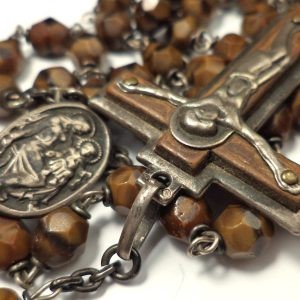 Close-up of antique rosary with brown banded agate beads, silver crucifix, and central medal.