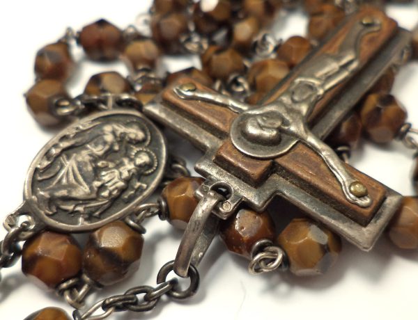 Close-up of antique rosary with brown banded agate beads, silver crucifix, and central medal.